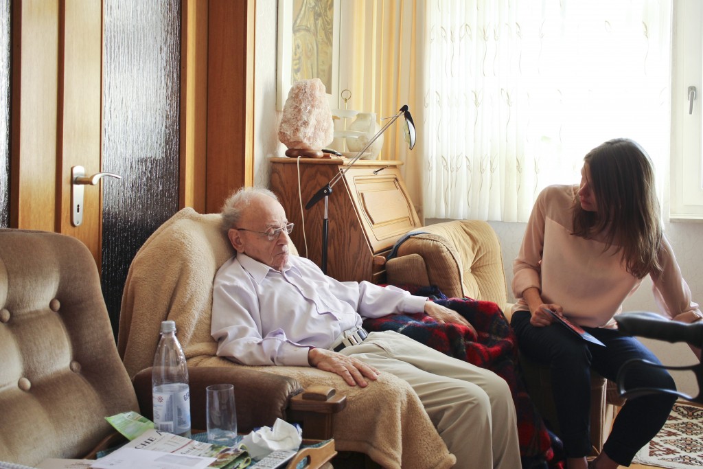 Der Holocaust-Überlebende Rolf Abrahamsohn sitzt in einem Sessel in seiner Wohnung, neben ihm Ruth Anne Damm, Gründerin des Vereins "Zweitzeugen"